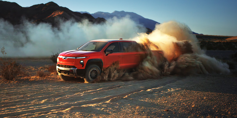 A 2026 Silverado EV Trail Boss driving through a vast desert landscape under a clear blue sky.